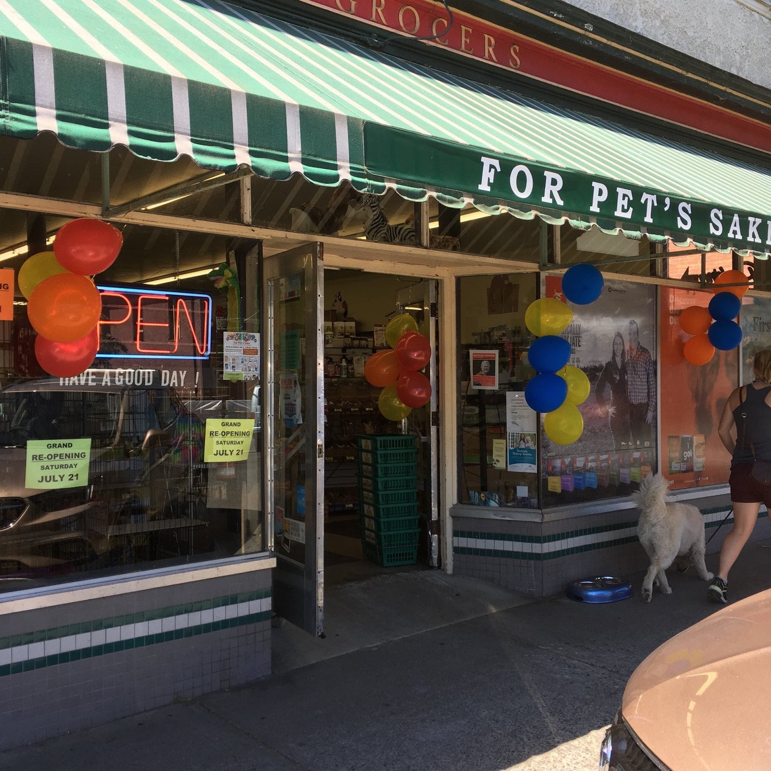 Storefront with a green and red striped awning, balloons, and a 'For Pet's Sake' sign.